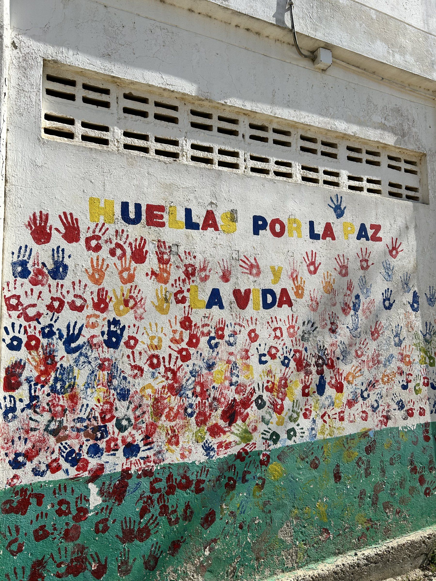 Mural Huellas por la paz y la vida, cubierto de manos pintadas en rojo, azul y amarillo